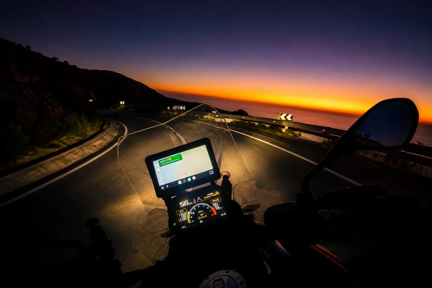 De nuit sur une route côtière : l'écran TFT et le GPS éclairent, les commandes au guidon restent dans le noir complet