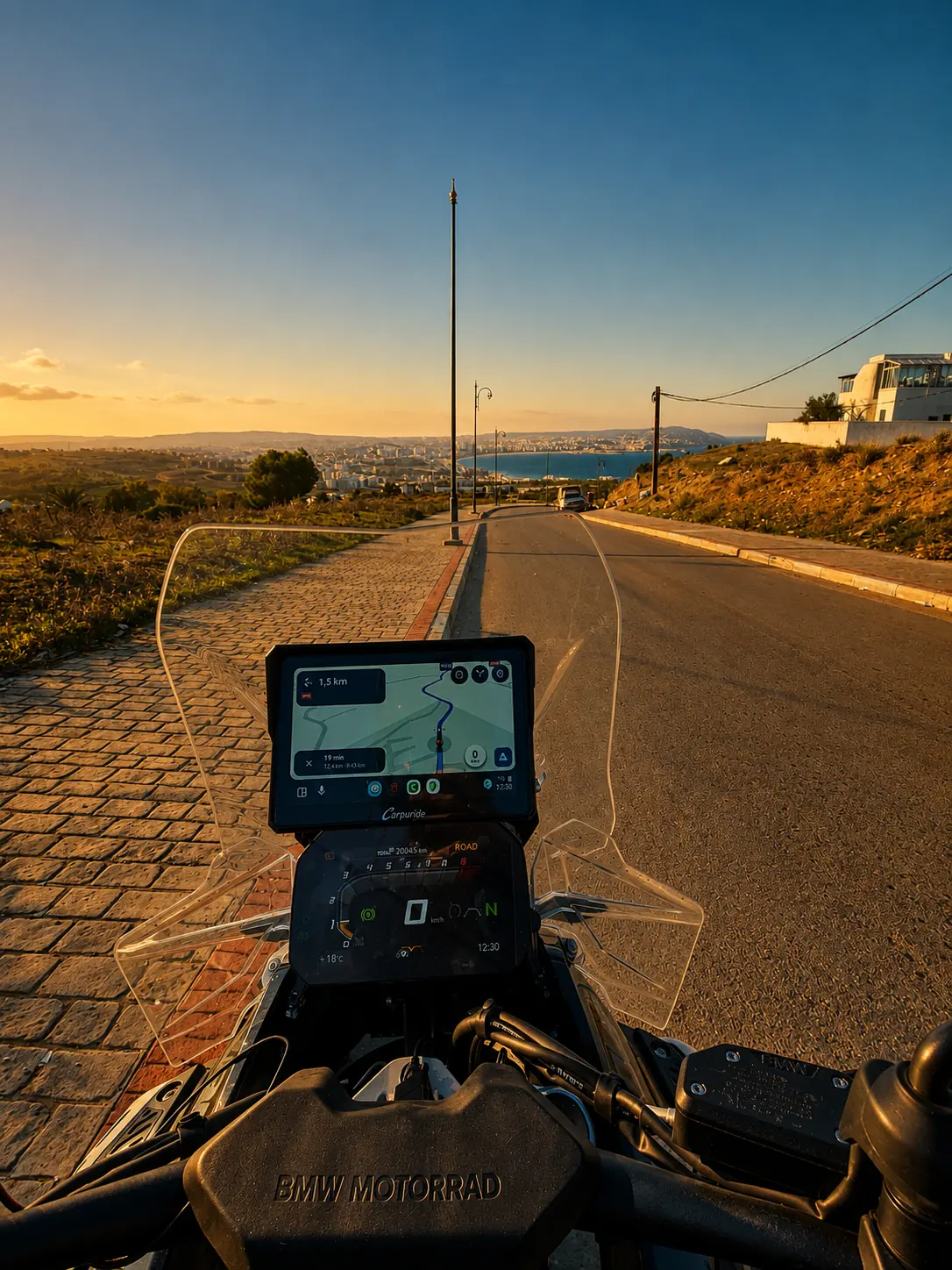 Depuis la selle, une route qui descend vers une baie et une ville côtière en lumière rasante